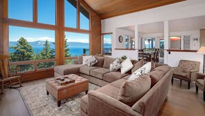 A spacious living room with large windows, a cozy seating area, and a view of the sea. - Dynamic Views, Hot Tub, Gym, 2nd Living Room, Garage and More. (Carnelian Bay)