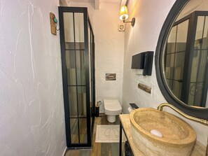 A bathroom with a glass door, a toilet, a sink with a round basin, and a mirror.