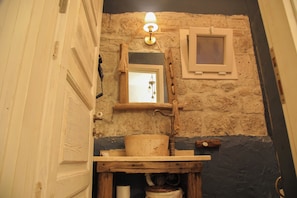 Bathroom features a stone wall, wooden door, and a window above the mounted mirror.