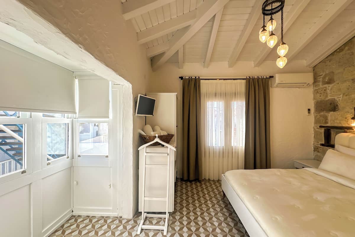 A bedroom with a bed, a TV on a stand, a wardrobe, and a window with curtains.