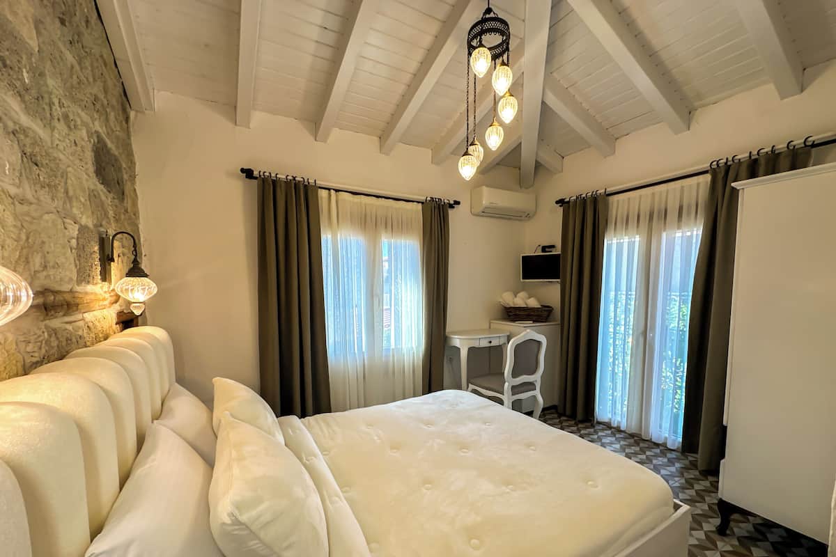 A bedroom with a bed, a desk, a chair, a TV, and a stone wall.