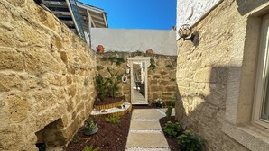 A narrow stone pathway leading to a door, flanked by stone walls and potted plants.