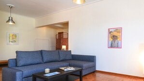 Ein modernes Wohnzimmer mit einem blauen Sofa, einem schwarzen Couchtisch und einem Holzboden im Fischgrätmuster.