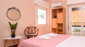 Ein Schlafzimmer mit Bett, Sessel, kleinem Tisch mit Pflanze, Klimaanlage und Fenster mit Aussicht.