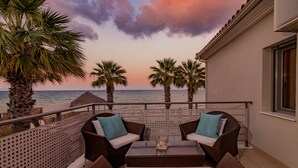 A balcony with wicker furniture, a table, and a view of the sea at sunset.