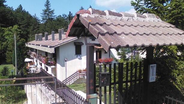 A rustic building with a tiled roof, a wooden fence, and a staircase leading to a balcony.