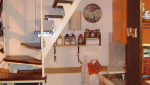 A kitchen with wooden stairs leading to a loft area, a clock on the wall, and various kitchen items on shelves.