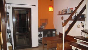 A room with a wooden door, a fireplace, a table, a chair, and a staircase.