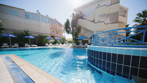 A swimming pool with lounge chairs and umbrellas, surrounded by buildings. - Artemis Comfort & Pleasure (Rhodes)
