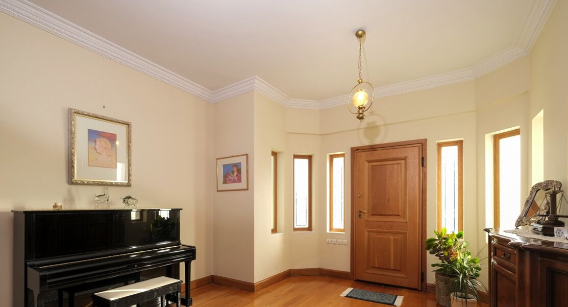 A room with a piano, framed artwork on the wall, a wooden door, and a potted plant.