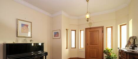 A room with a piano, framed artwork on the wall, a wooden door, and a potted plant.