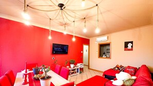 Una sala de estar moderna con una decoración en tonos rojos, una zona de comedor con una mesa de madera y sillas rojas, y un rincón de estar acogedor con un sofá rojo y cojines.