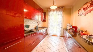 Una cocina con armarios rojos, piso de baldosas, lámpara colgante y ventana con cortinas estampadas.