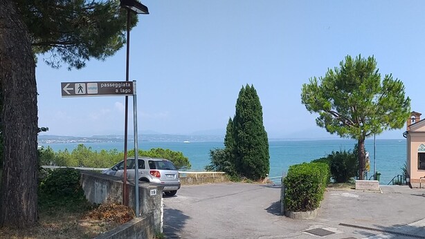 Un estacionamiento con un letrero que indica un sendero peatonal hacia el mar.