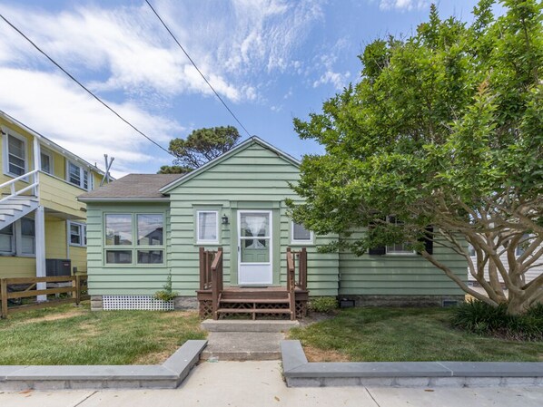 A single-story house with a front porch, a small front yard, and a tree to the right.