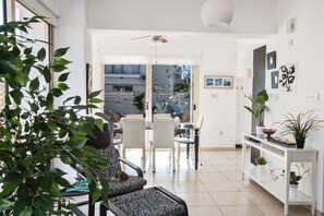 Ein modernes Wohnzimmer mit Essbereich, weißen Möbeln und Blick durch Glastüren nach draußen.