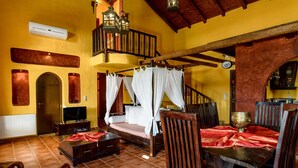 A spacious room with a large bed, a dining table, and a staircase leading to an upper level.