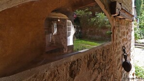 Une arche en pierre offrant une vue sur un jardin et un bâtiment situé à l’extérieur.