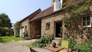 Un bâtiment en pierre avec une cour en gravier, des sièges en plein air et des plantes en pot.