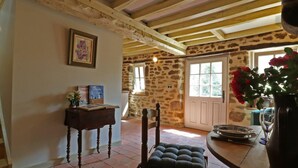 Un intérieur rustique avec un mur en pierre, des poutres en bois, une chaise en bois, une petite table avec des livres et un vase rempli de fleurs.