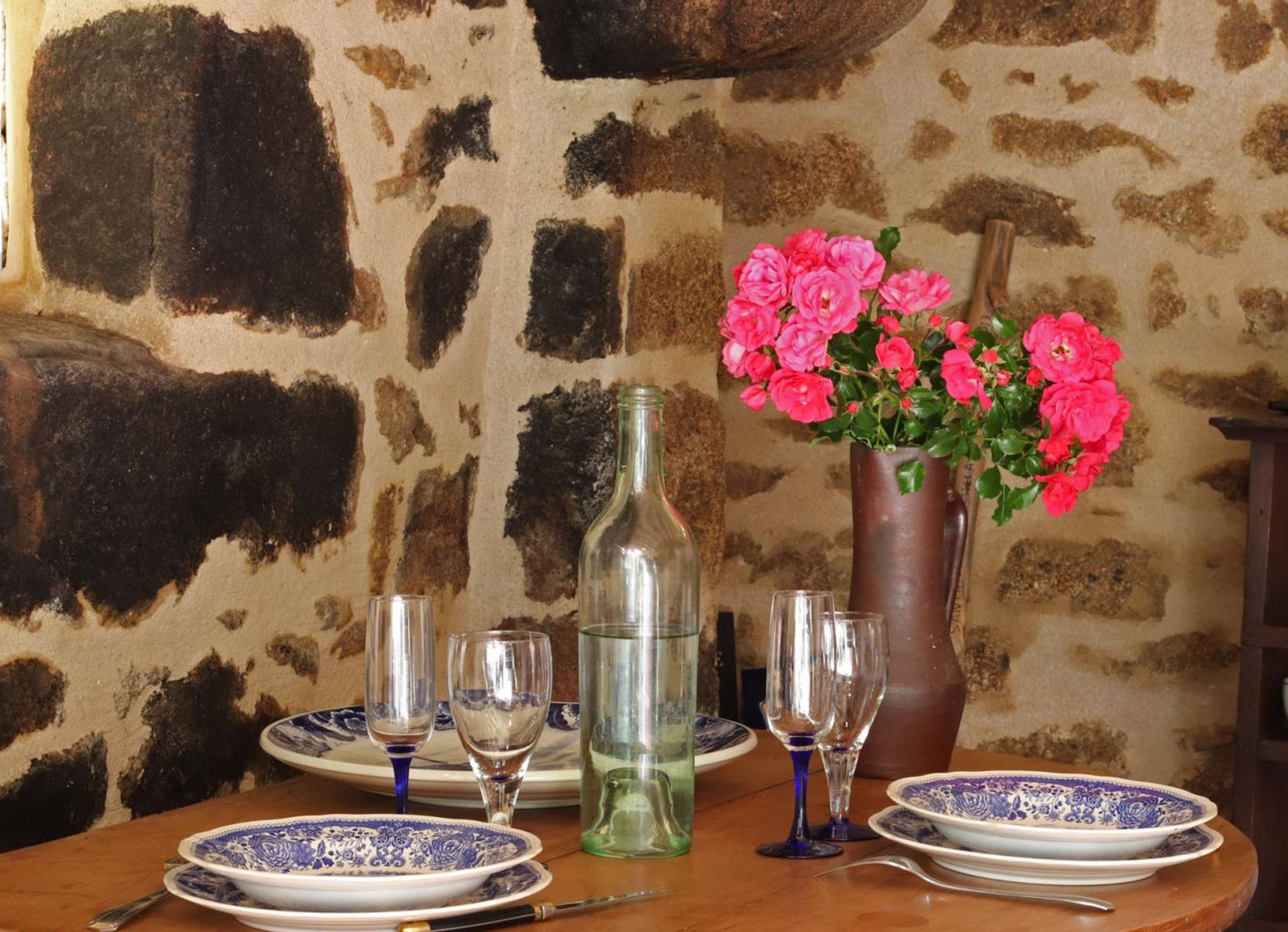 A table set with blue and white patterned plates, clear wine glasses, and a vase with pink flowers.