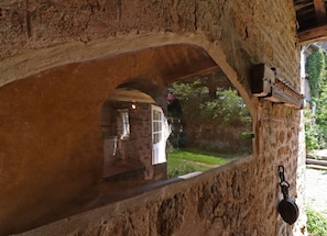 A stone archway with a view of a garden and a building outside.