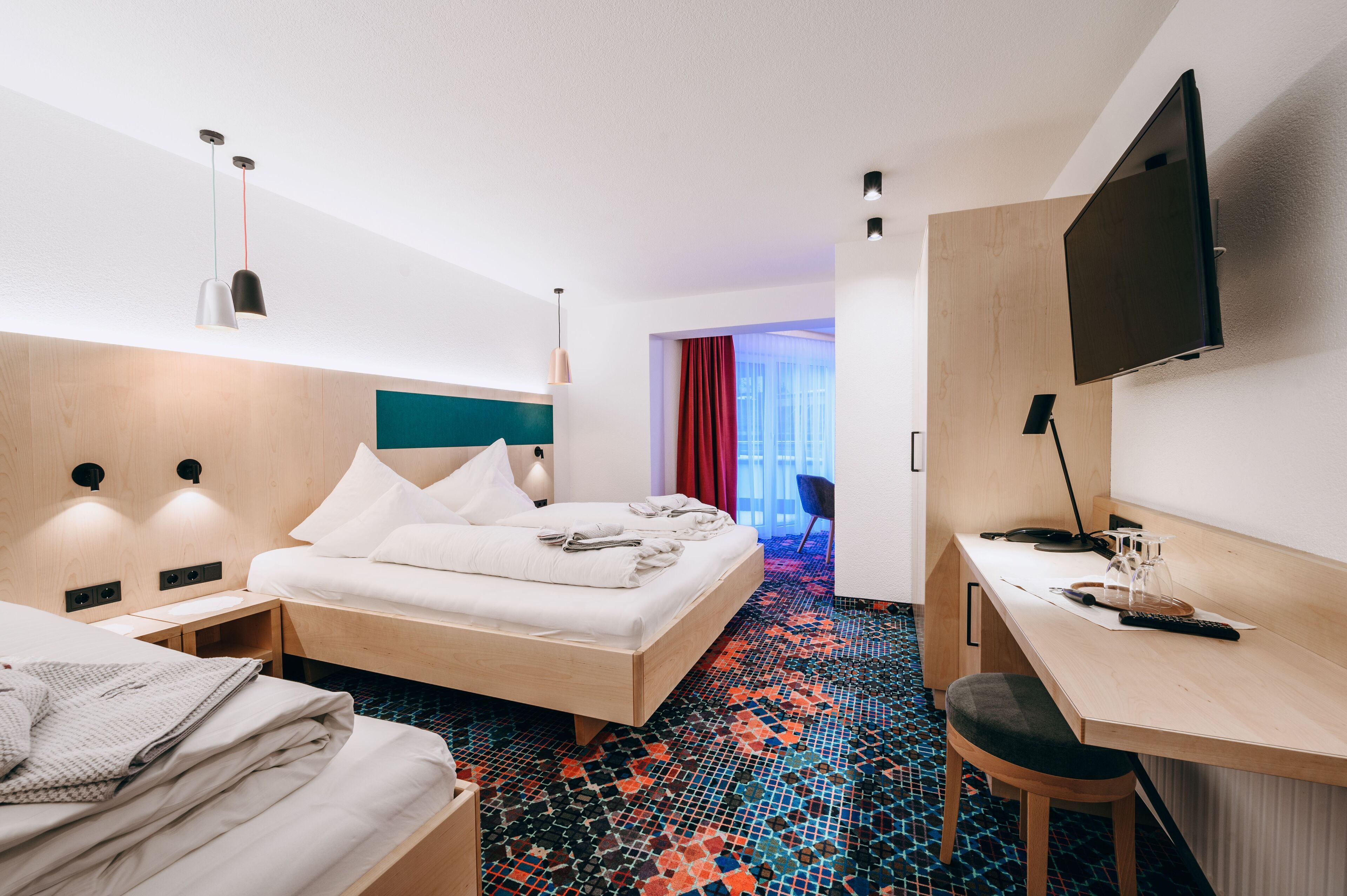 A hotel room with a bed, desk, TV, and a colorful tiled floor.