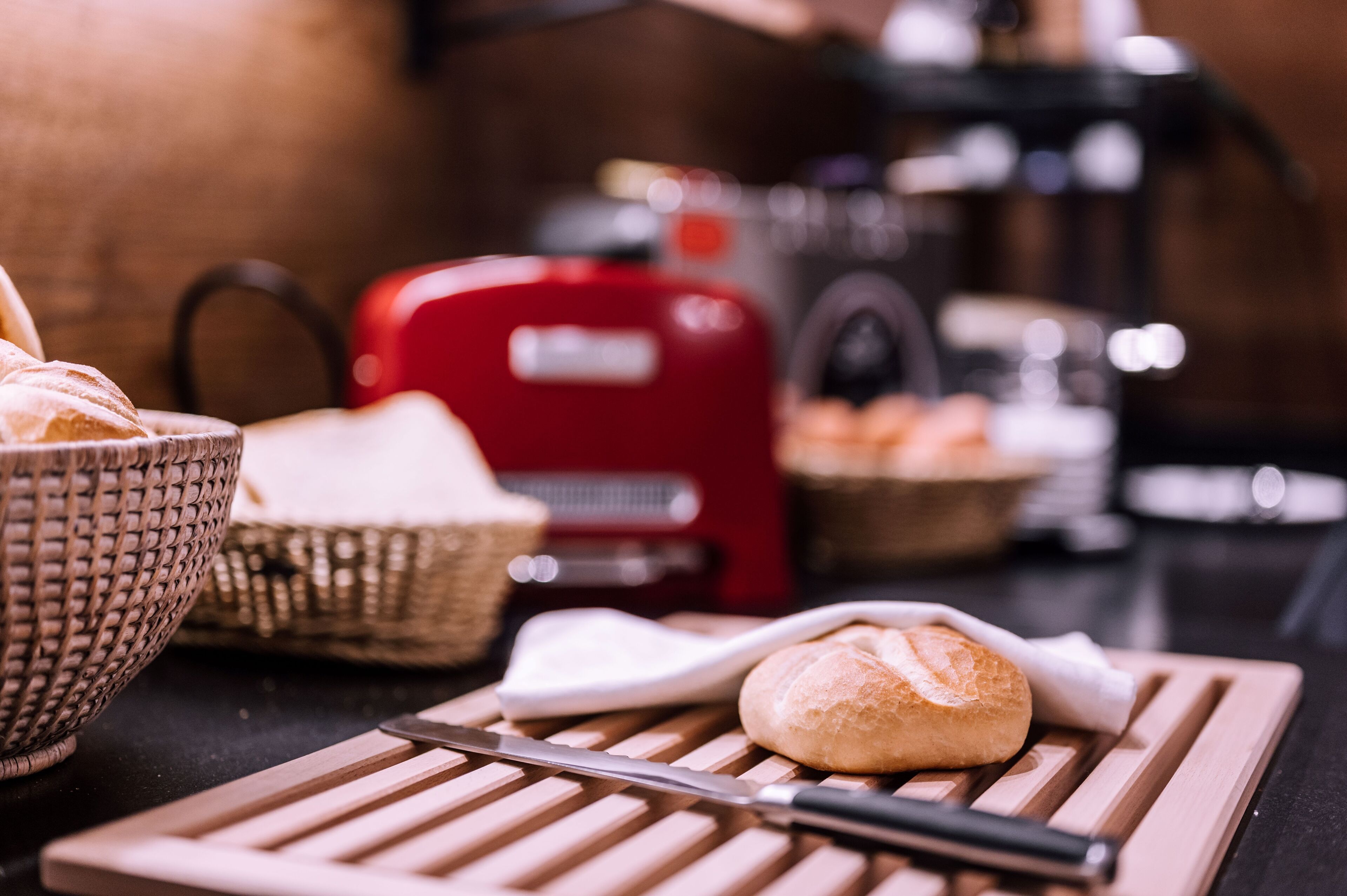 A kitchen counter with a loaf of bread, a knife, a red appliance, and a woven basket.