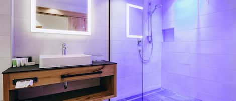 A modern bathroom with a glass shower enclosure, a wooden vanity with a sink, and a mirror with integrated lighting.