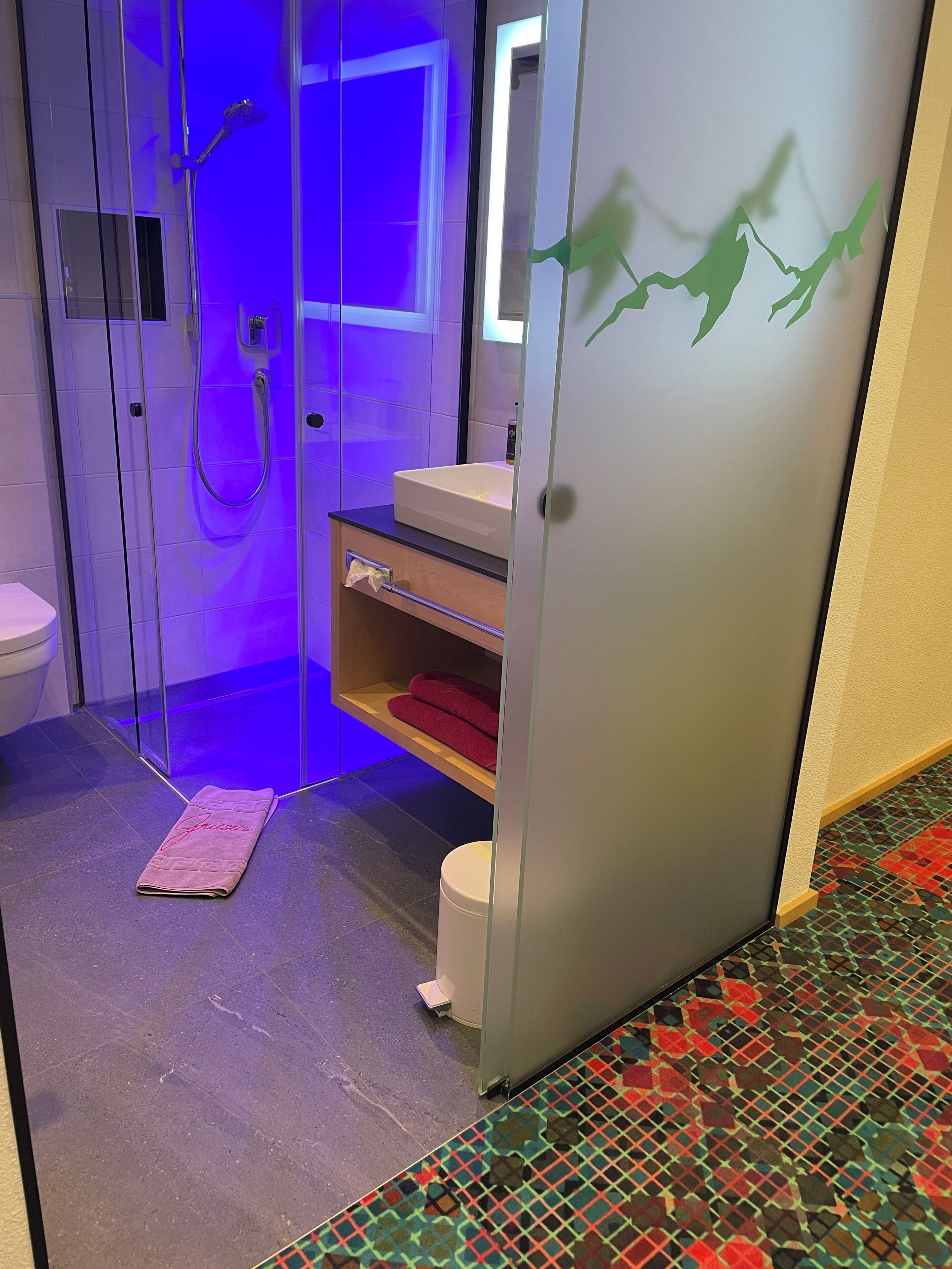 A modern bathroom with a glass-enclosed shower, a white sink, and a red towel on a shelf.