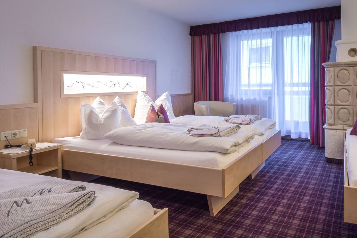 A hotel room with two beds, a desk, a chair, and a large window with curtains.