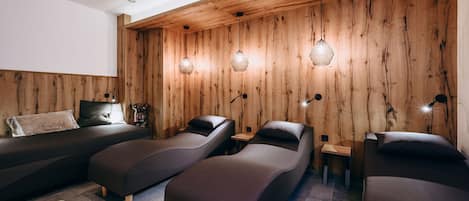 Un moderno spa con paredes de madera, tres camillas de masaje oscuras e iluminación colgante.