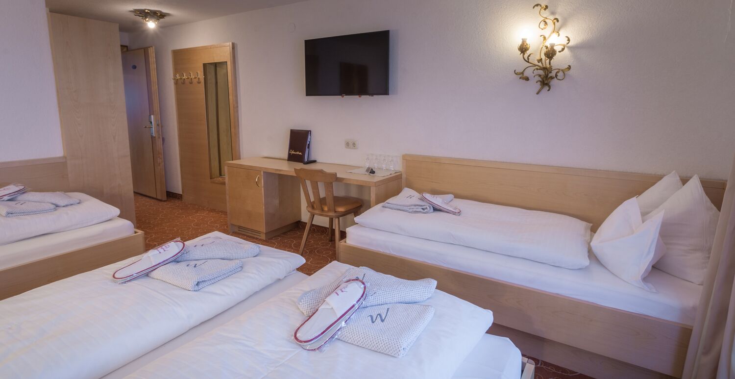 Habitación de hotel con dos camas, un escritorio, una silla, un televisor y una lámpara fijada a la pared.