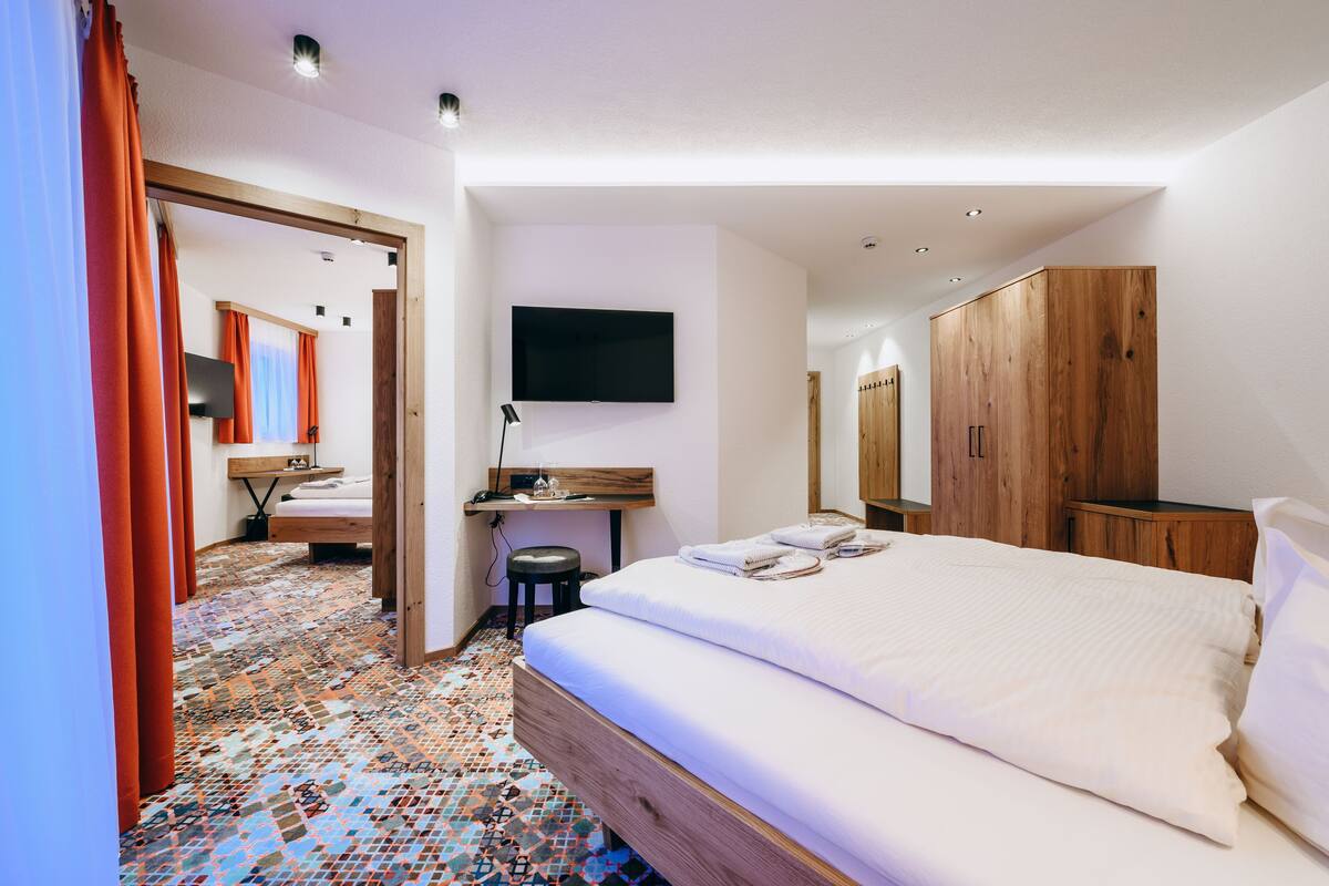 A hotel room with a large bed, a desk with a chair, a TV mounted on the wall, and a wardrobe.