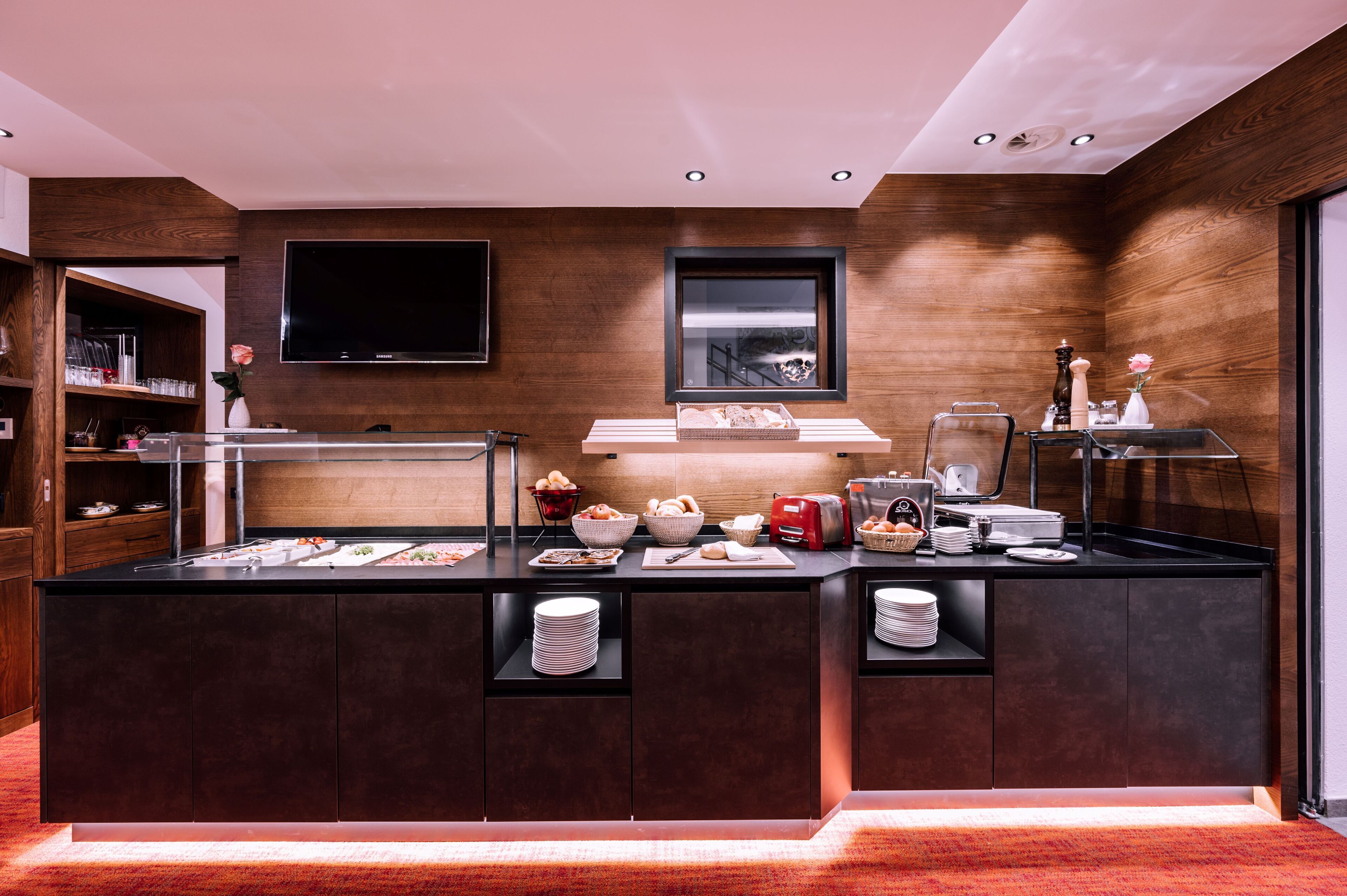 A modern kitchen with a central island, built-in shelves, and a flat-screen TV.