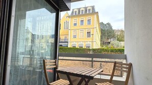 Ein Balkon mit Holztisch und Stühlen, einer Glastür und Blick auf ein gelbes Gebäude.