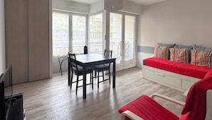 Ein Zimmer mit Esstisch, Stühlen, einer Couch mit bunten Kissen, einem Fernseher und großen Fenstern mit Blick.
