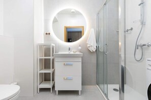 Ein modernes Badezimmer mit einer einteiligen Duschkabine, einem weißen Waschtisch mit rundem Spiegel und einer Toilette.