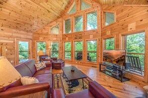 A cozy cabin interior with a wooden interior, large windows, a sofa, a table, and a fireplace.