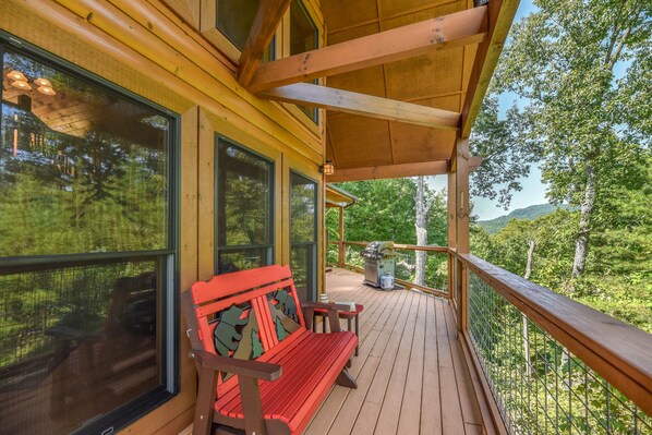A wooden deck with a bench and a grill, overlooking a forested area.