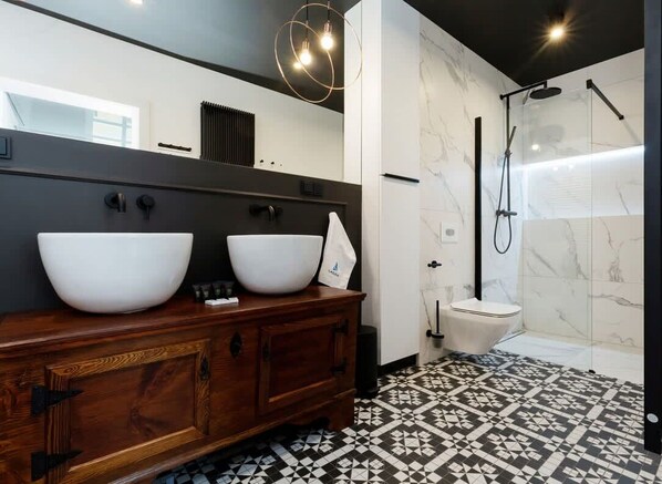 Un baño moderno con dos lavamanos grandes de color blanco, un mueble de tocador de madera, un inodoro y una zona de ducha con cabina de vidrio.
