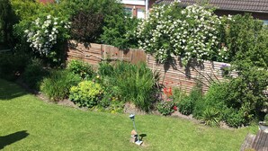 Ein gepflegter Garten mit Rasenmäher, umgeben von einem Holzzaun und verschiedenen blühenden Pflanzen.