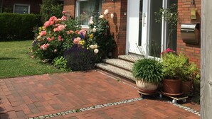 Ein Ziegelhaus mit Ziegeldach, einer Haustür und einer kleinen Veranda mit Blumentöpfen und Blumen.