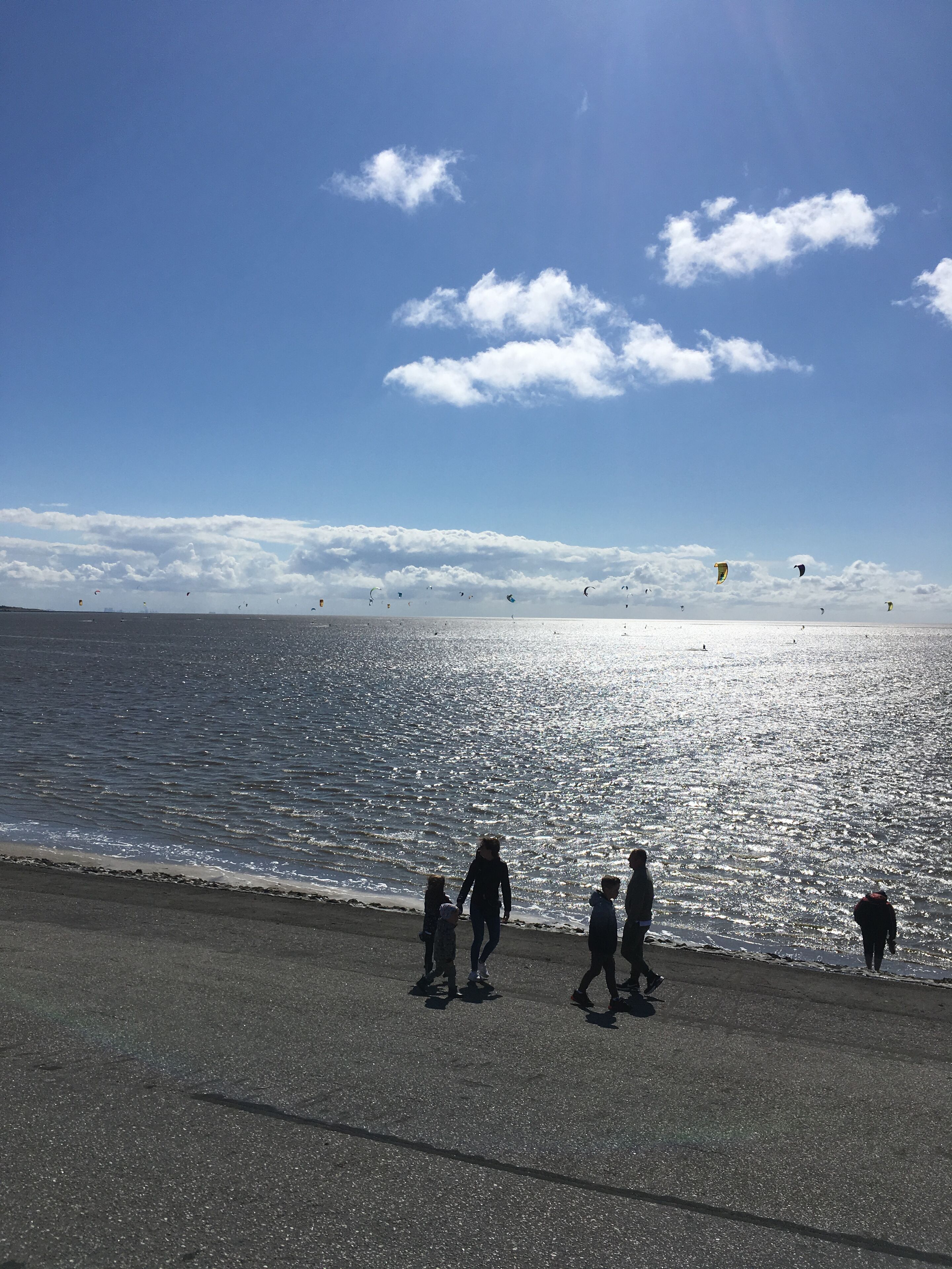 A beach with a clear sky, people walking along the shore, and kites flying in the distance.