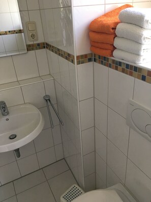 A bathroom with a sink, a shower, and a stack of towels.