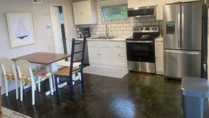 A modern kitchen with white cabinets, a stainless steel refrigerator, a built-in oven, and a dining area with a table and chairs.