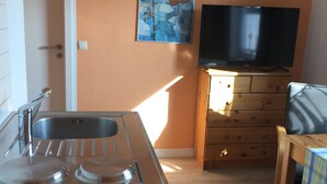 Una cocina con un lavamanos, estufa y armarios de madera. Hay un televisor sobre un soporte de madera y un cuadro en la pared.