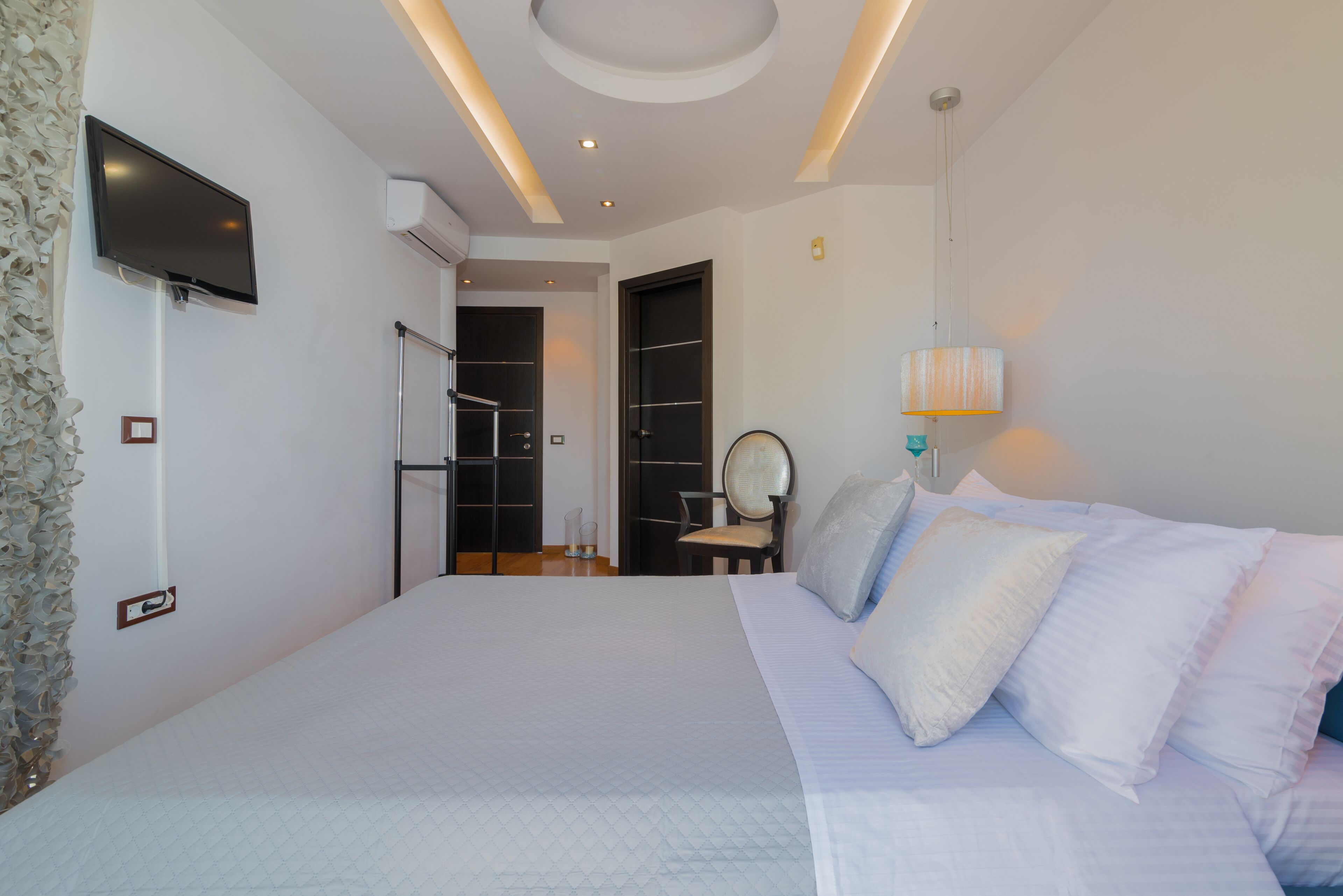 Ein modernes Schlafzimmer mit einem großen Bett, einem flachbildfernseher an der Wand und einer Deckenleuchte.