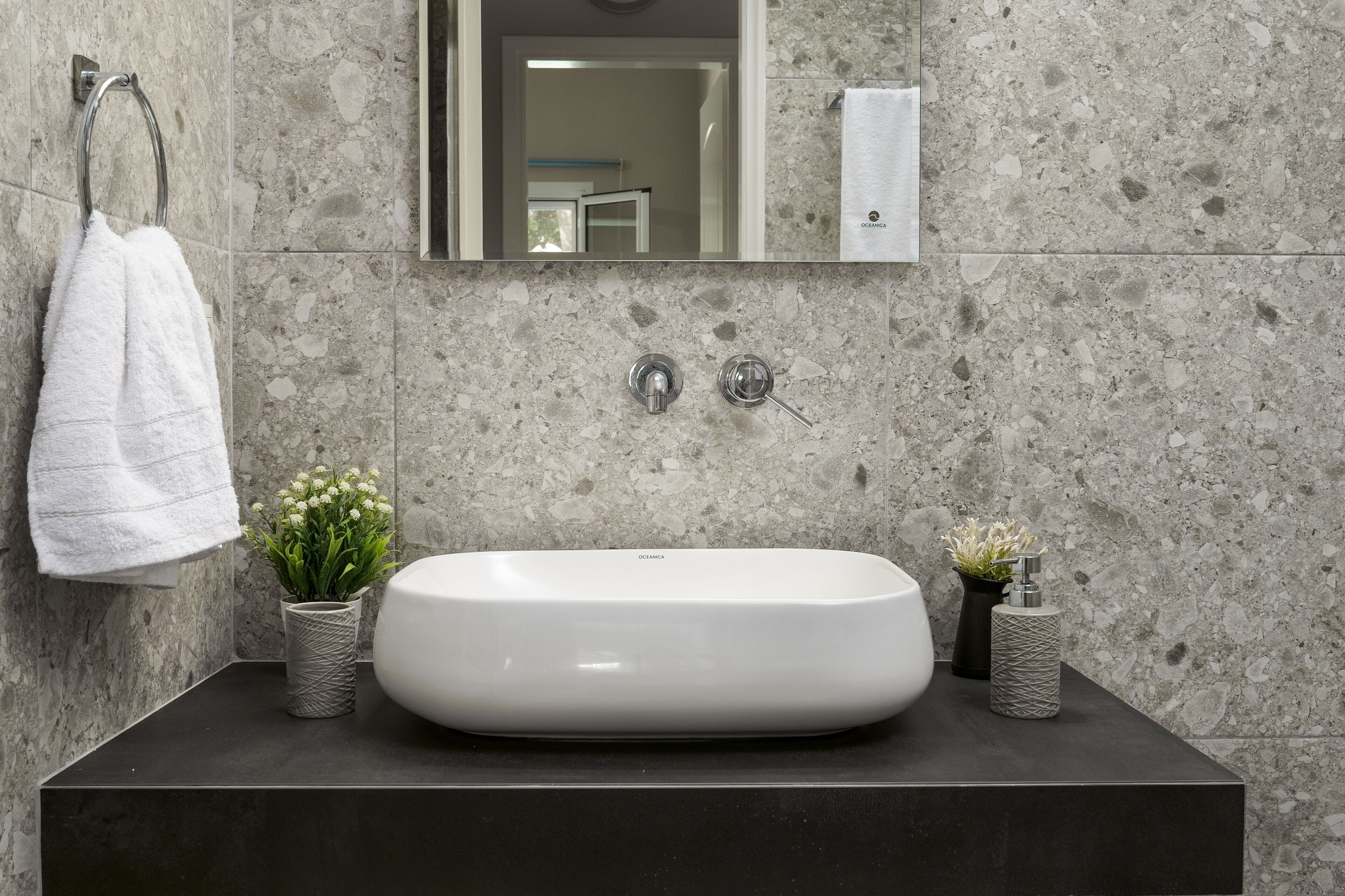 A bathroom with a large white sink, two faucets, a towel rack, and two small potted plants.