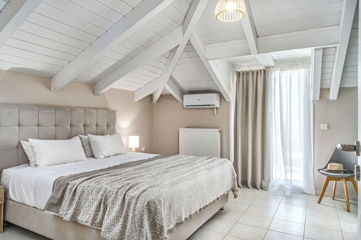 A bedroom with a large bed, a nightstand, a lamp, a radiator, and a window with curtains.